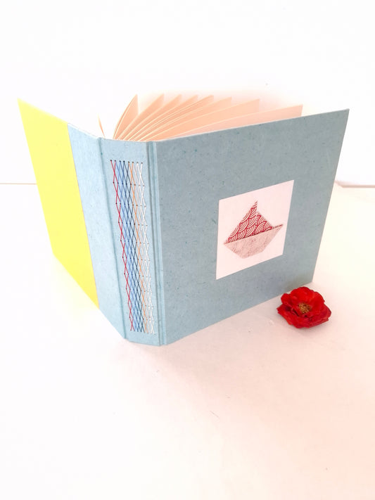 Album nascita con barca origami in rosso, celeste e miele